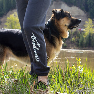 Model posing in grey sweatpants with travel nurse logo below the knee. dog in background
