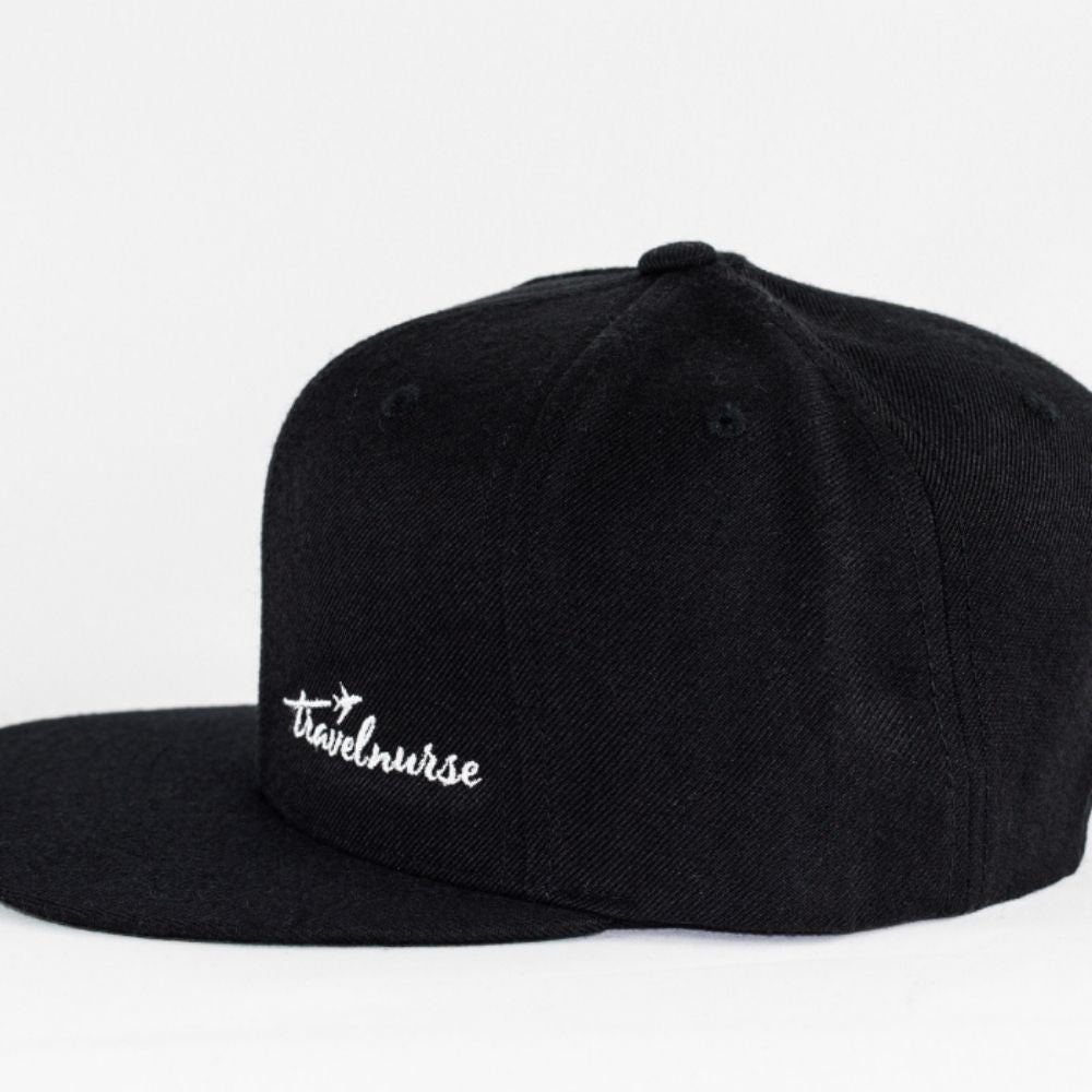 Product photo showing a black snapback with a white travel nurse logo