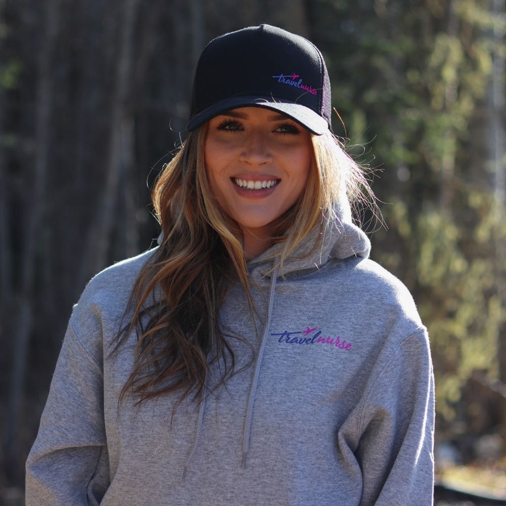 from view of a model wearing a sweatshirt and hat. Both have the travel nurse logo in pink and blue