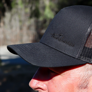 Man wearing a black mesh back hat with a black travel nurse logo